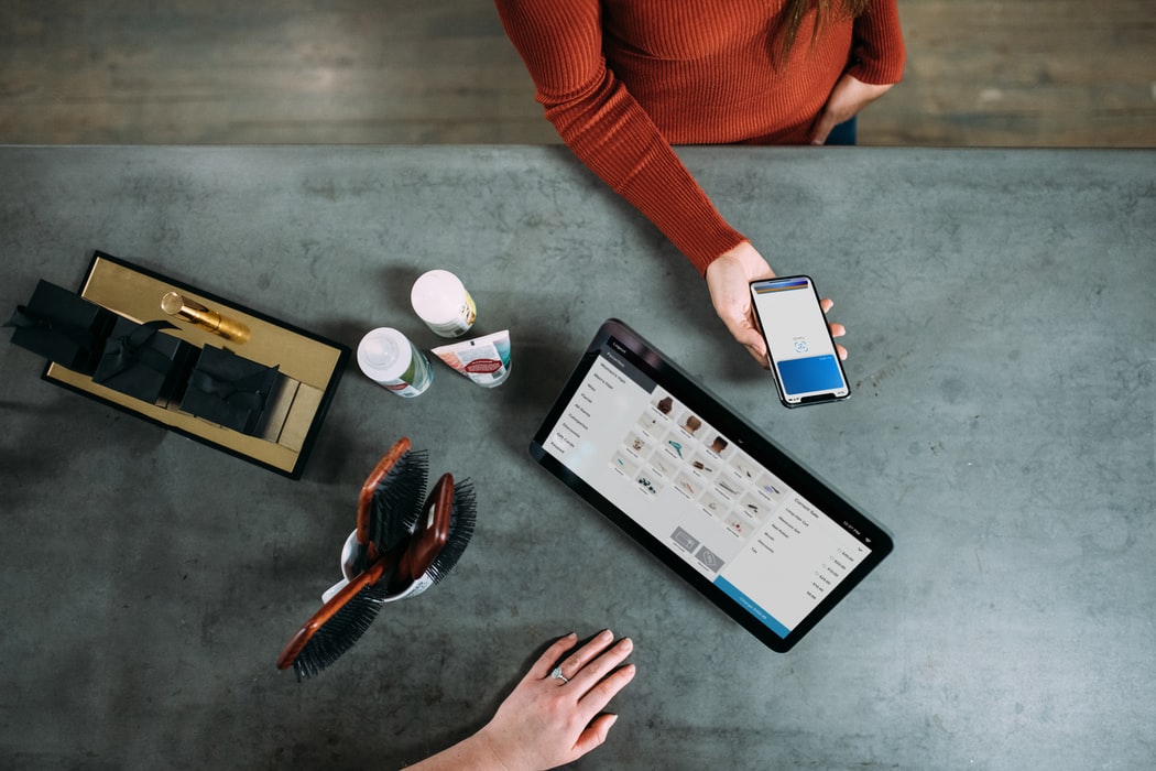 woman holding smartphone near tablet at counter with shop merchandise