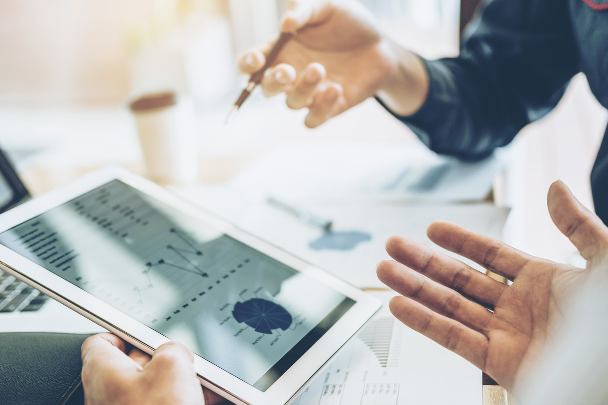 close-cropped-photo-of-two-people's-hands-gesturing-at-tablet-showing-data-graphs-of-partnership