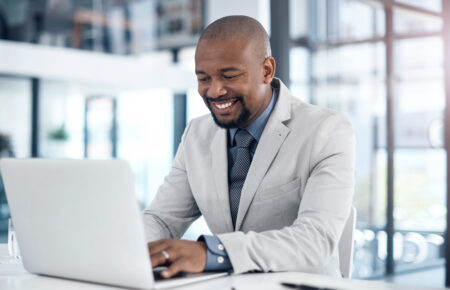 Businessman using a laptop to process Automated Clearing House transactions in a modern office.